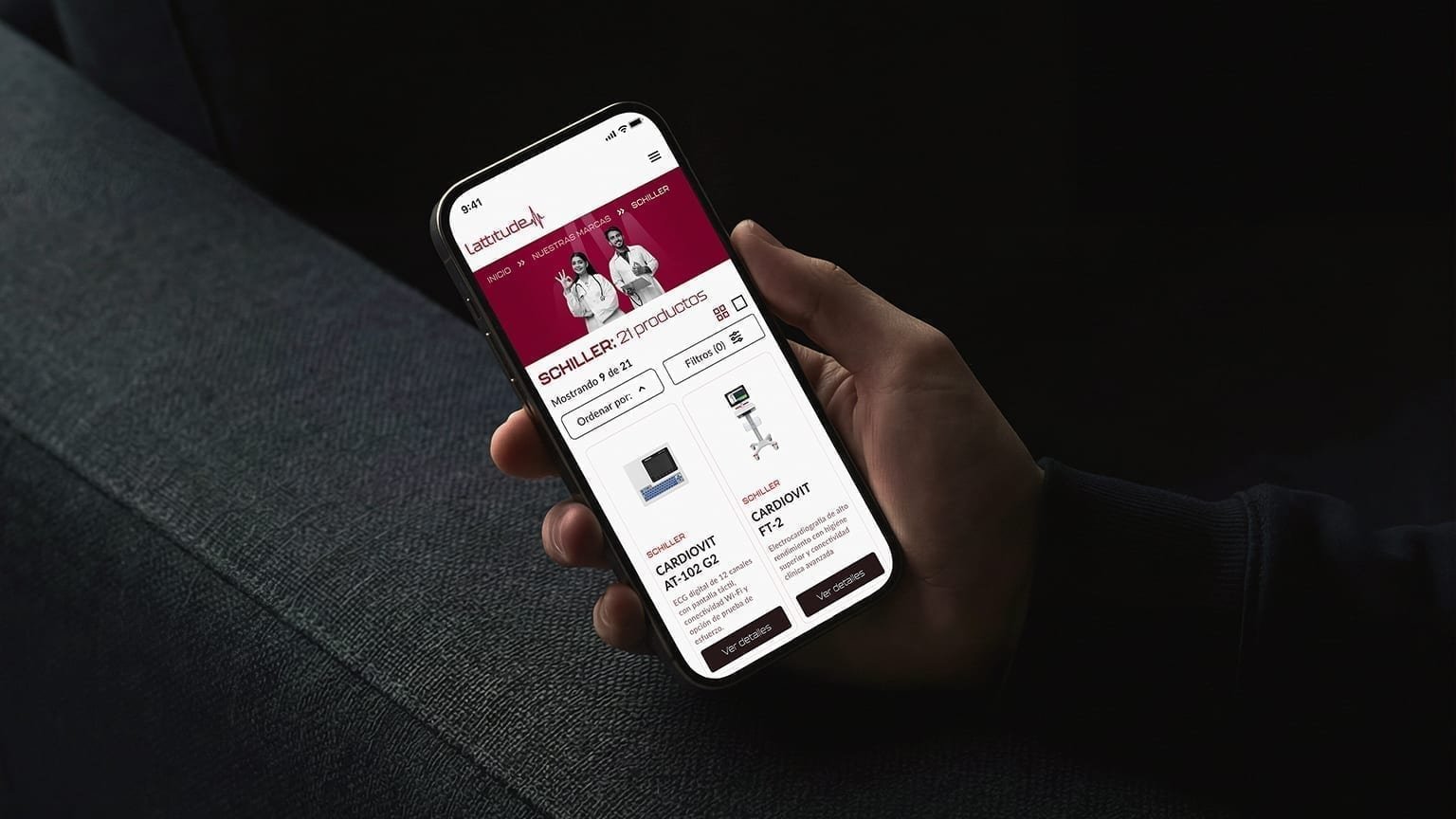 Hand holding a phone showing the Lattitude mobile Schiller catalog with CARDIOVIT AT-102 G2 and FT-2 product cards.