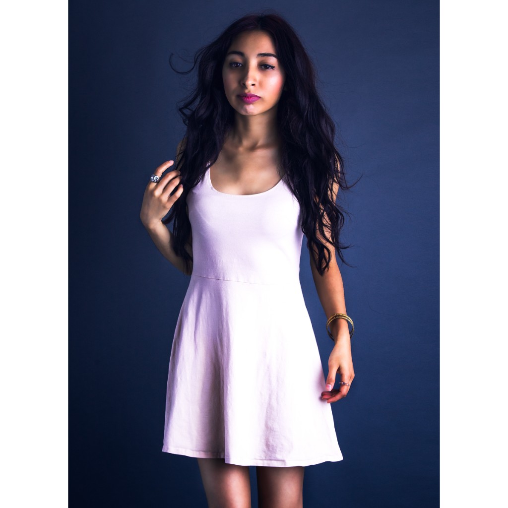 Alondra fashion portrait: pale pink sleeveless skater dress, silver statement ring and gold bangle, hand in hair; full-length pose on navy studio backdrop — commercial talent portrait.