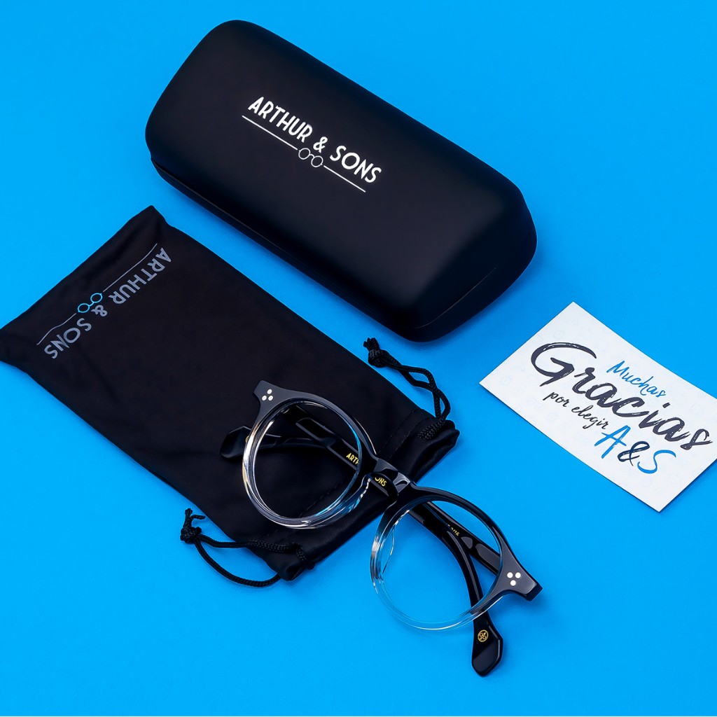 Grayscale flat lay: trial frame with black occluders, mixed lenses, and partial grey case; reflective white surface. Arthur & Sons Mexico collection — photograph 117 of 119.