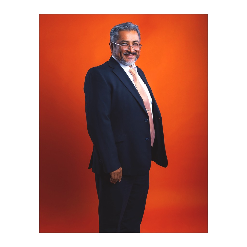 Doto executive portrait: man in navy suit, white shirt and peach tie, orange studio background.