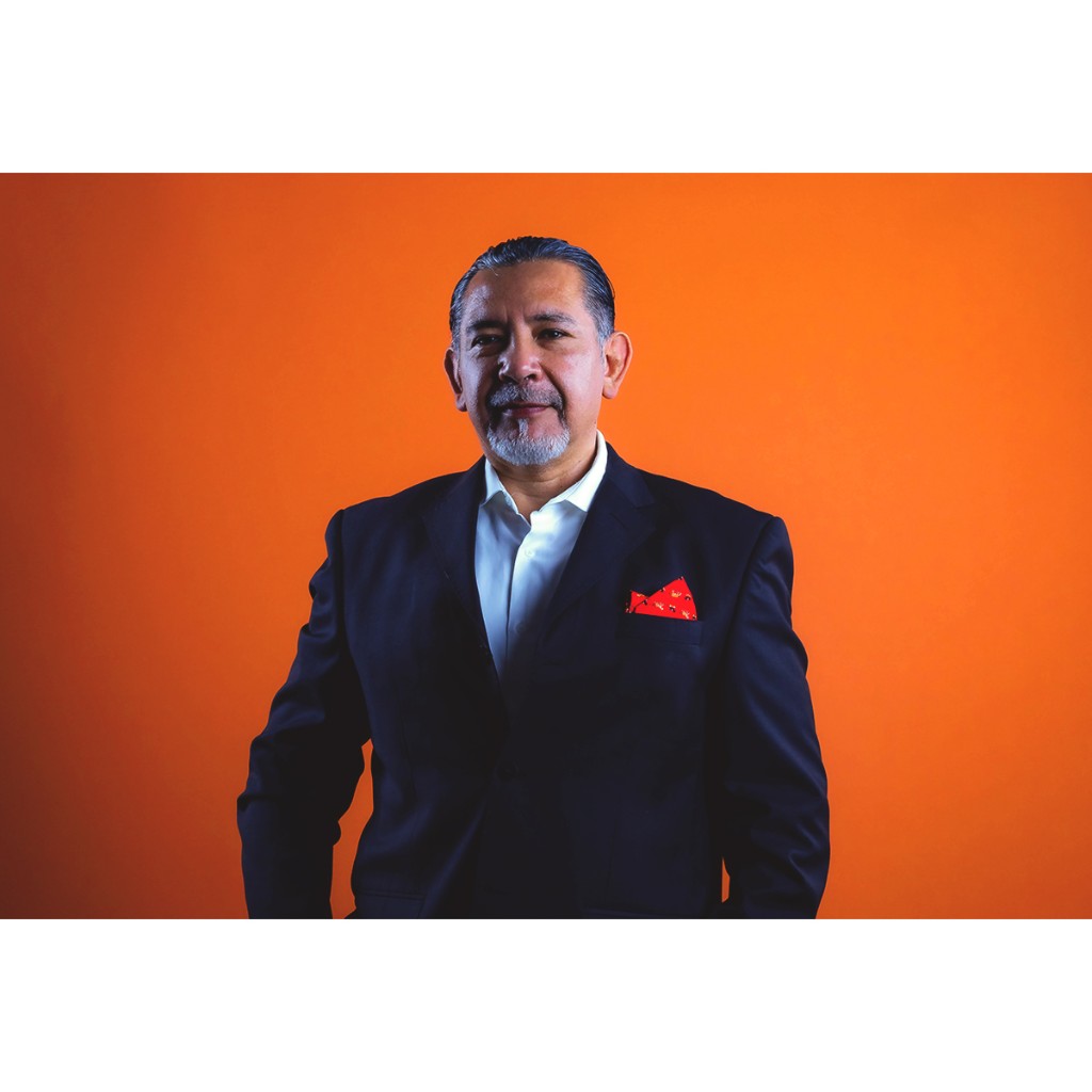 Doto executive portrait: man in dark suit, white shirt and red pocket square, orange backdrop.