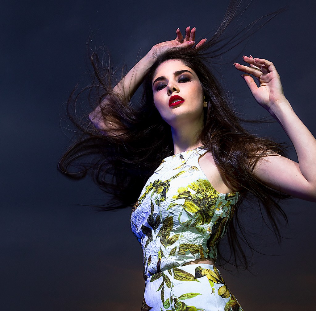 Ferezing fashion portrait: long hair in motion, white botanical top, smoky eyes and red lip, dark set with cool rim light.