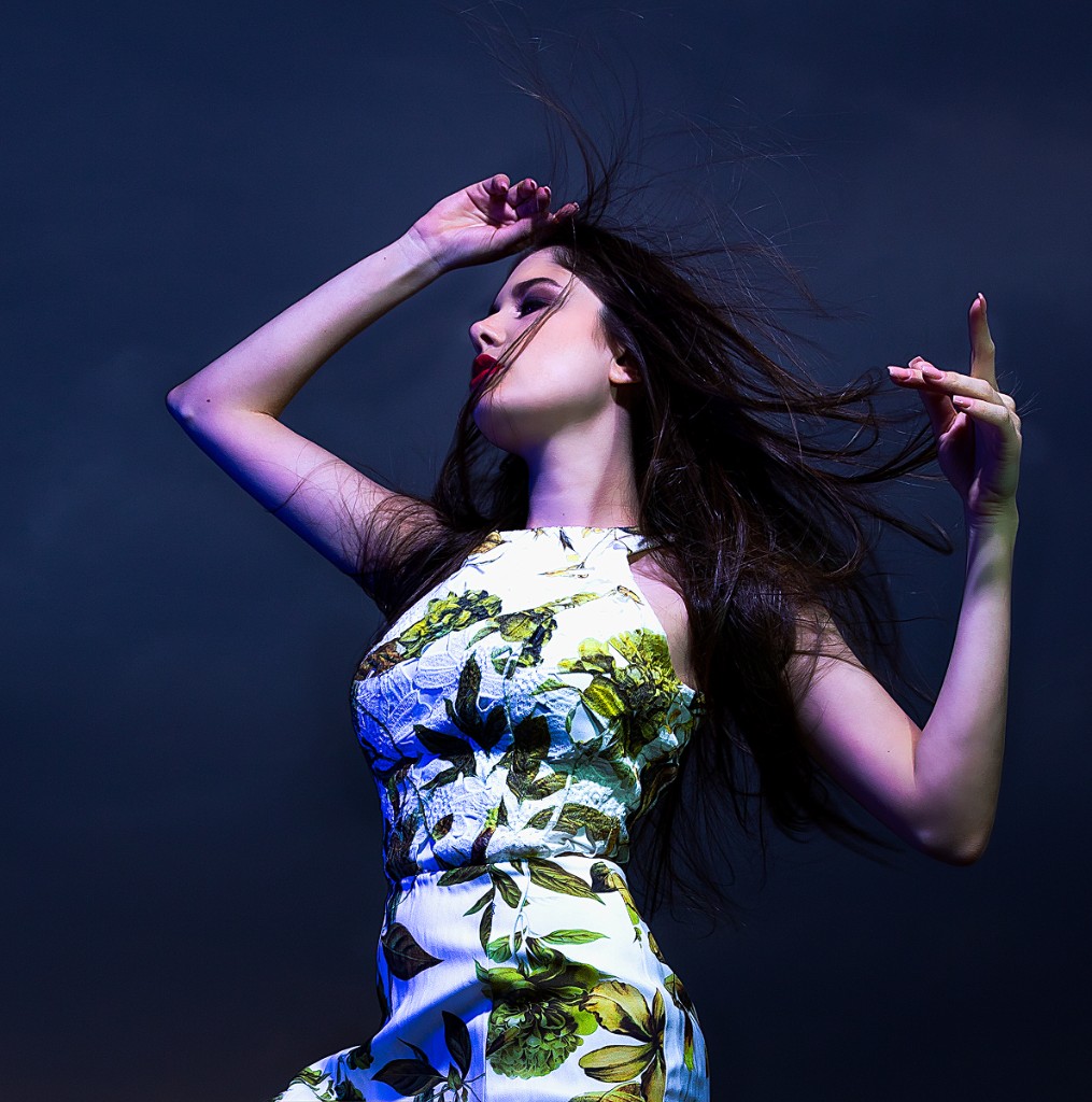 Ferezing editorial profile: green-and-yellow floral dress, dynamic hair and arms, blue-magenta accent light on deep blue background.