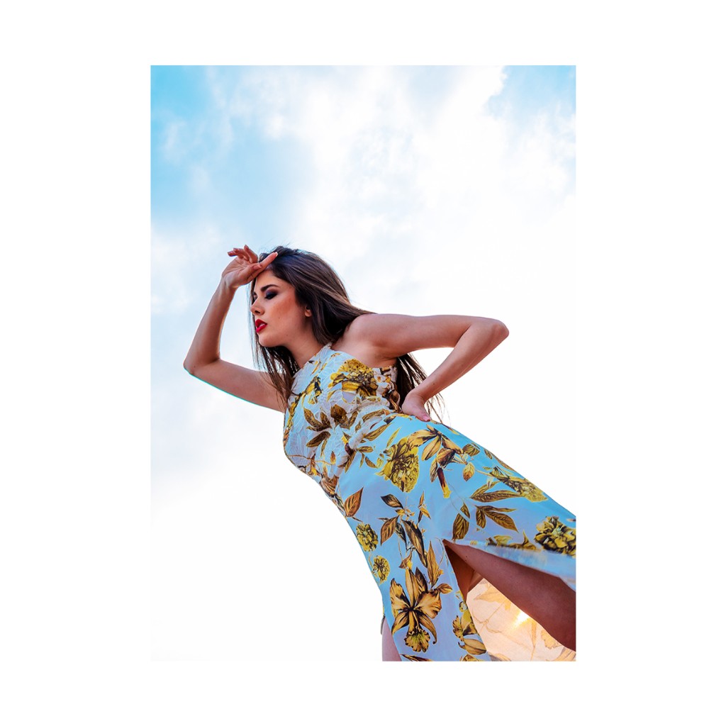 Ferezing fashion: halter floral dress with side slit, hand at forehead and on hip, warm outdoor light.
