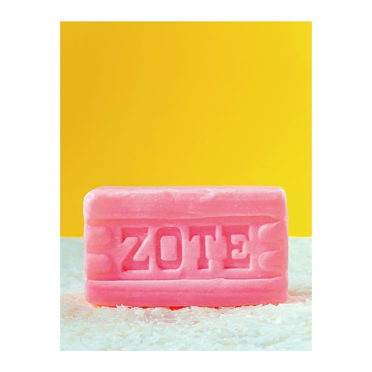Pink Zote laundry bar with embossed ZOTE on white soap shavings and yellow backdrop. “100 Years of History” editorial project, Fábrica de Jabón La Corona — piece 12 of 38.