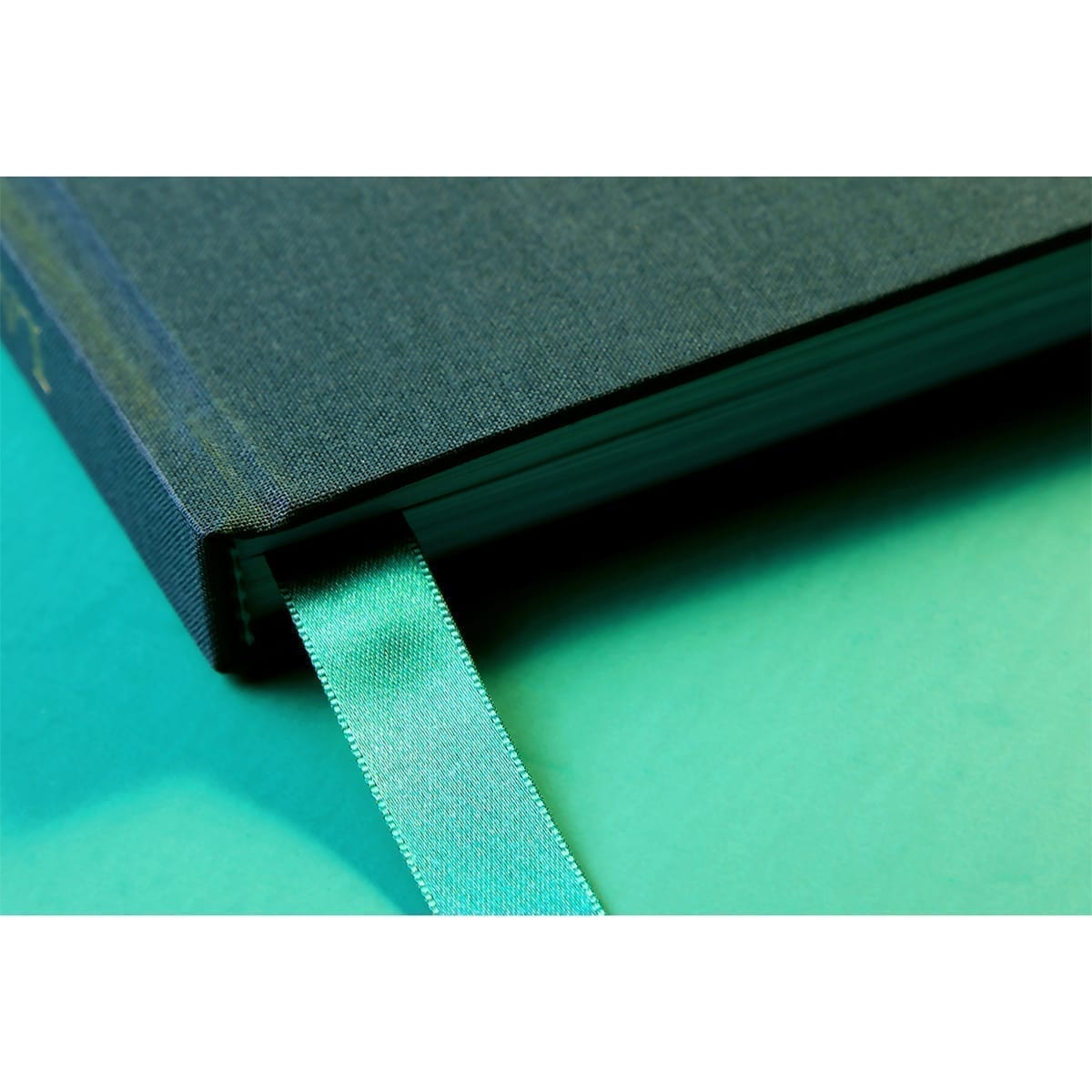 Close-up of a closed green cloth book corner with a green ribbon bookmark; mint surface. “100 Years of History” editorial project, Fábrica de Jabón La Corona — piece 25 of 38.