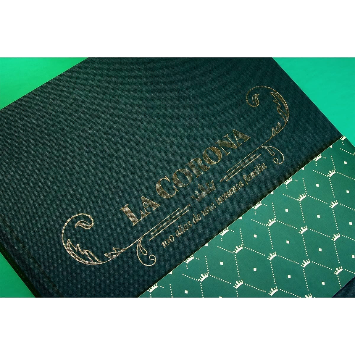 Cover “LA CORONA — 100 años de una inmensa familia” on green cloth with gold foil and crown-pattern belly band. “100 Years of History” editorial project, Fábrica de Jabón La Corona — piece 26 of 38.