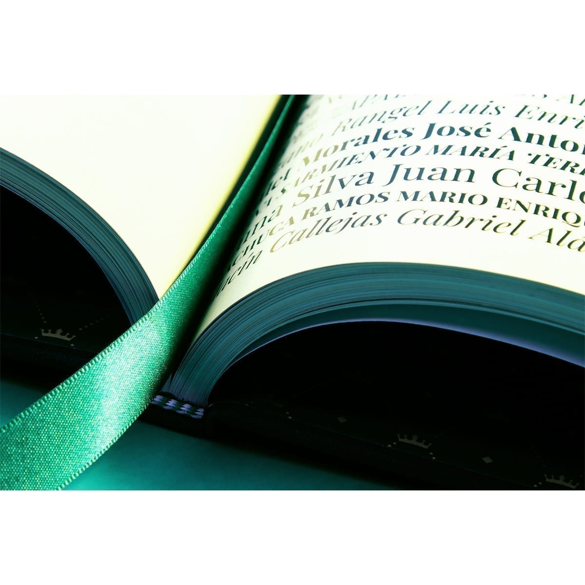 Open book: serif name list and green ribbon bookmark on crown-pattern endpapers. “100 Years of History” editorial project, Fábrica de Jabón La Corona — piece 29 of 38.