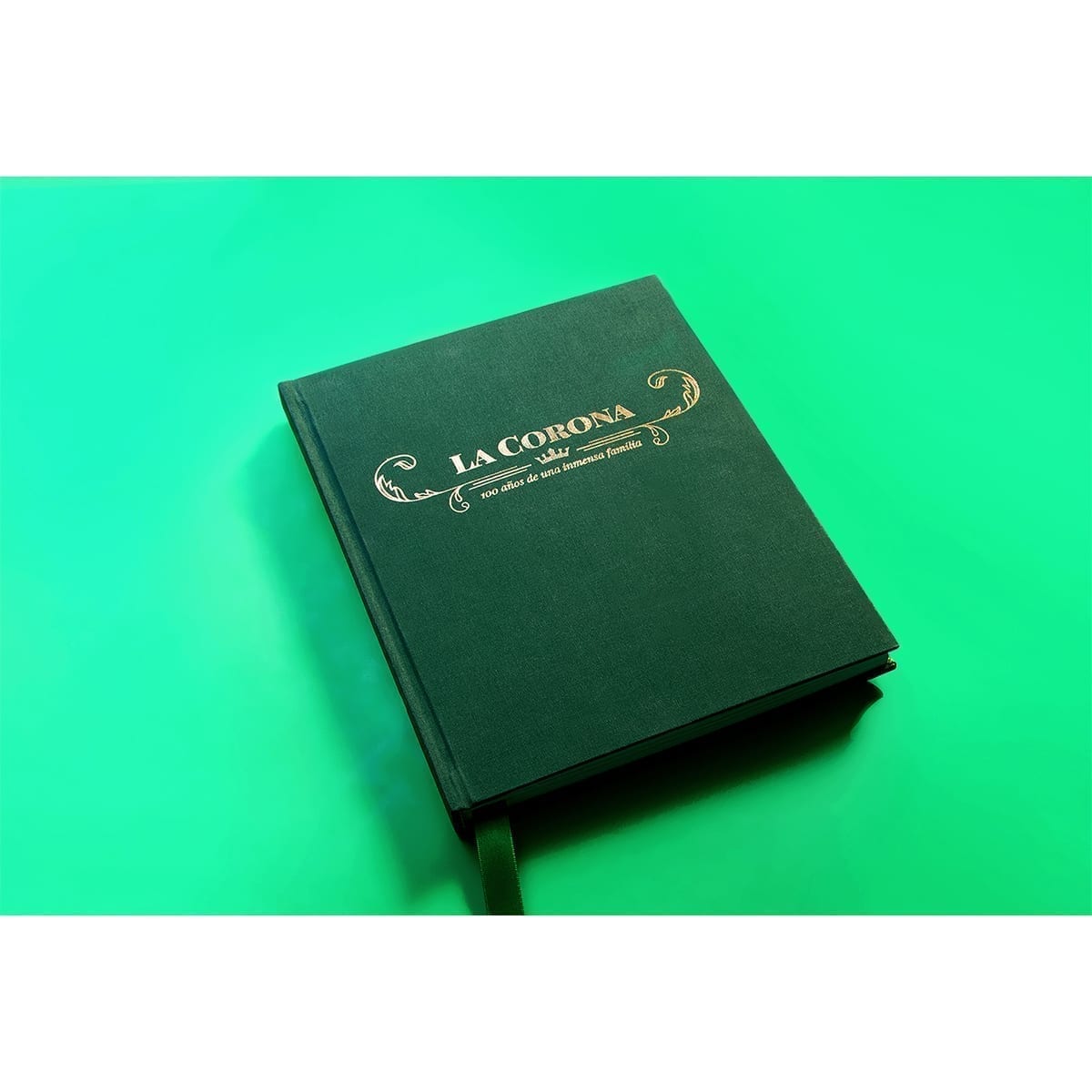 Closed book on the diagonal on lime green; gold LA CORONA cover and ribbon. “100 Years of History” editorial project, Fábrica de Jabón La Corona — piece 34 of 38.