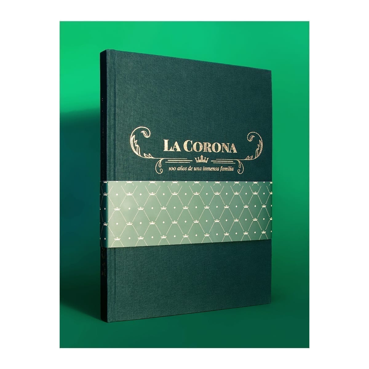 Standing hardcover: green cloth, gold foil, mint belly band, visible spine; green gradient backdrop. “100 Years of History” editorial project, Fábrica de Jabón La Corona — piece 38 of 38.