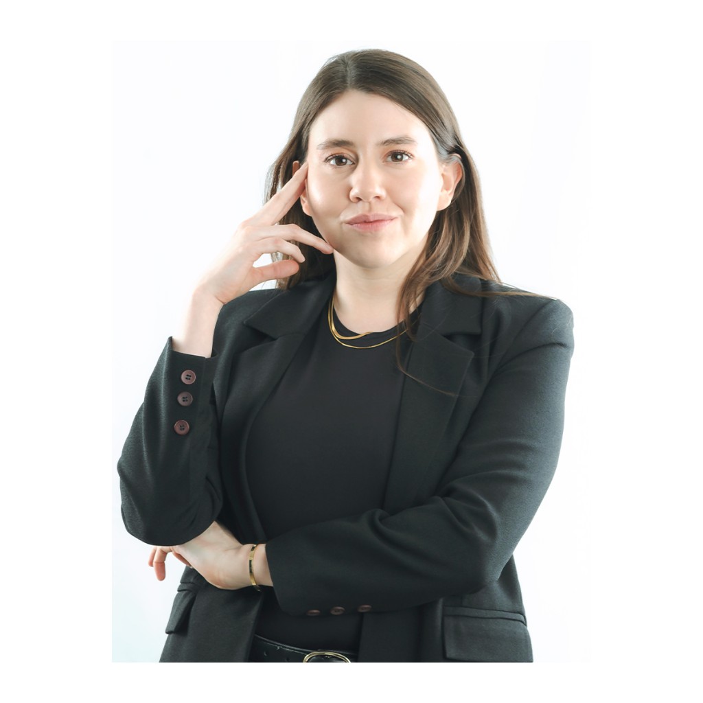 Liz Stryke commercial portrait: oversized black blazer, black tee, gold chain and bangle bracelet, hand at temple with a confident look; white high-key backdrop — personal brand headshot.