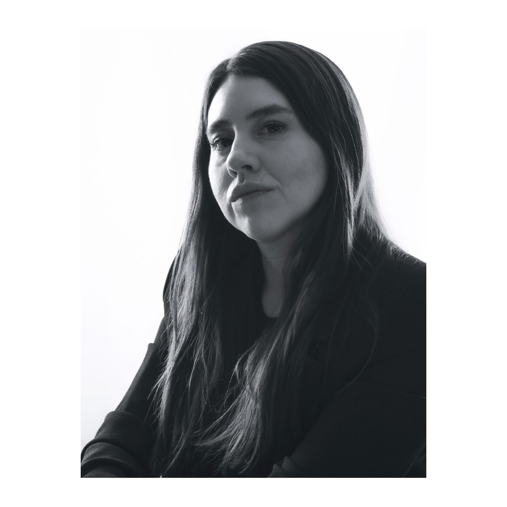 Liz Stryke B&W close-up: black top, long dark hair and upward contemplative gaze; side light on white background — editorial talent portrait.