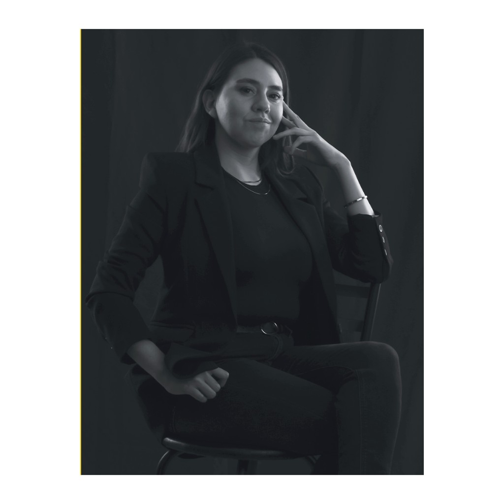 Liz Stryke B&W studio portrait: black blazer, hand at cheek and subtle smile; fine silver bracelet; three-quarter framing on dark background — commercial talent photography.