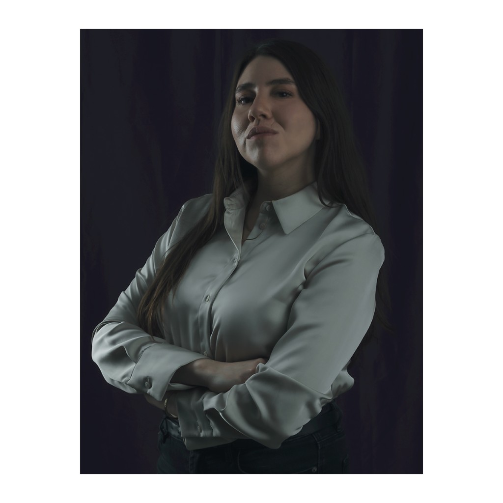Liz Stryke executive color portrait: sage green satin button-down blouse, arms crossed and dark jeans; serene upward gaze against dark purple curtain — personal brand commercial photography.