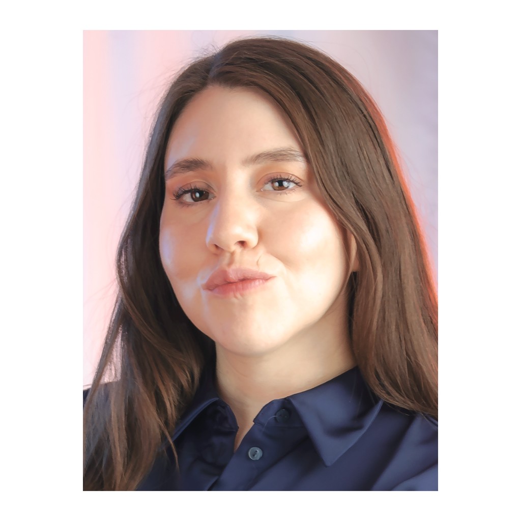 Liz Stryke glamour headshot: navy satin shirt, tight facial close-up with puckered lips and detailed makeup; warm orange light in hair on pink-lavender pastel background — talent casting photography.