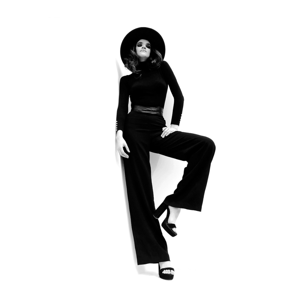Naty Velázquez full-length B&W editorial: hat, turtleneck, high-waist wide-leg trousers, belt and platform sandals against white set.