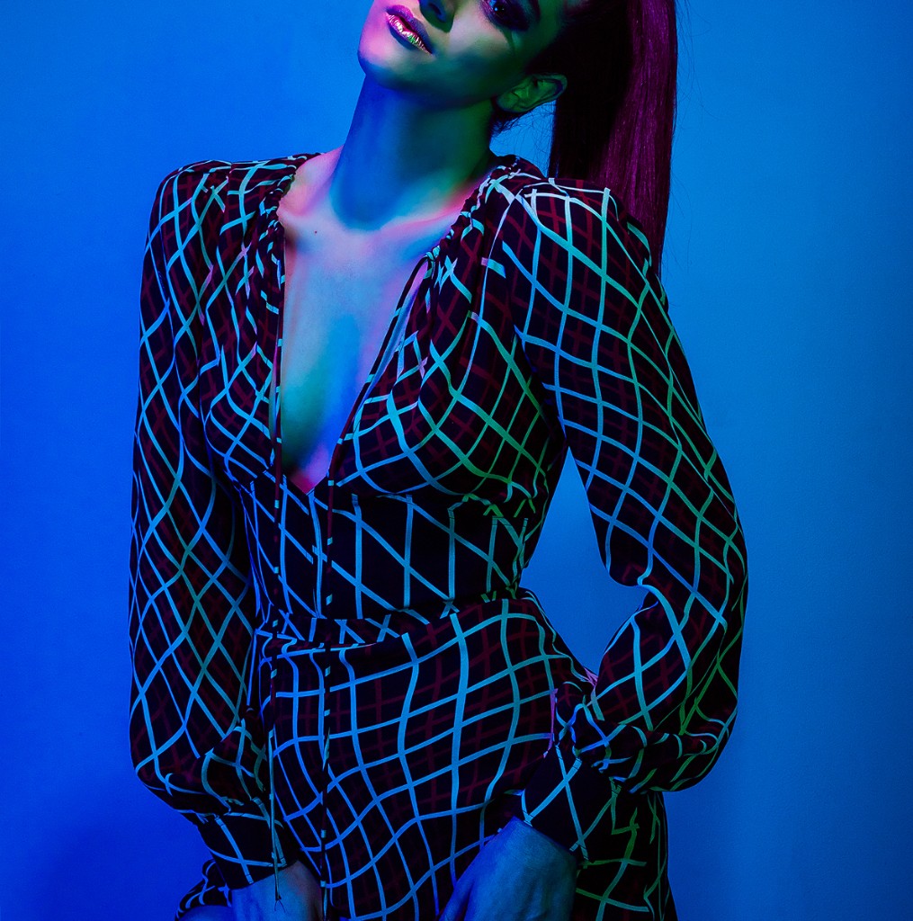 Naty Velázquez fashion portrait: lattice-pattern deep V-neck dress, blue and magenta gel lighting on blue set.